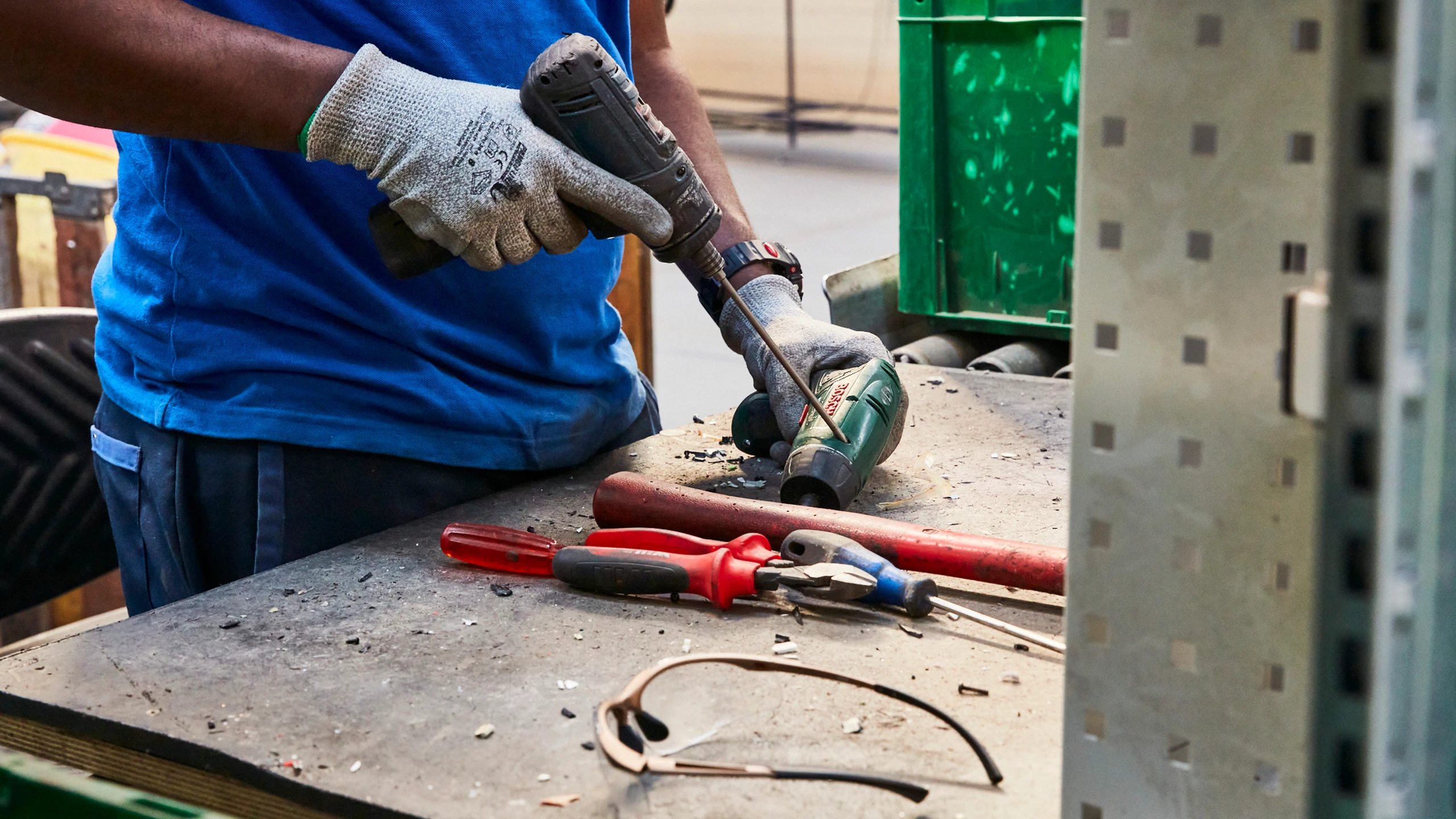 Galloo medewerker boort schroeven los op werkbank; handgereedschap en veiligheidsbril in beeld